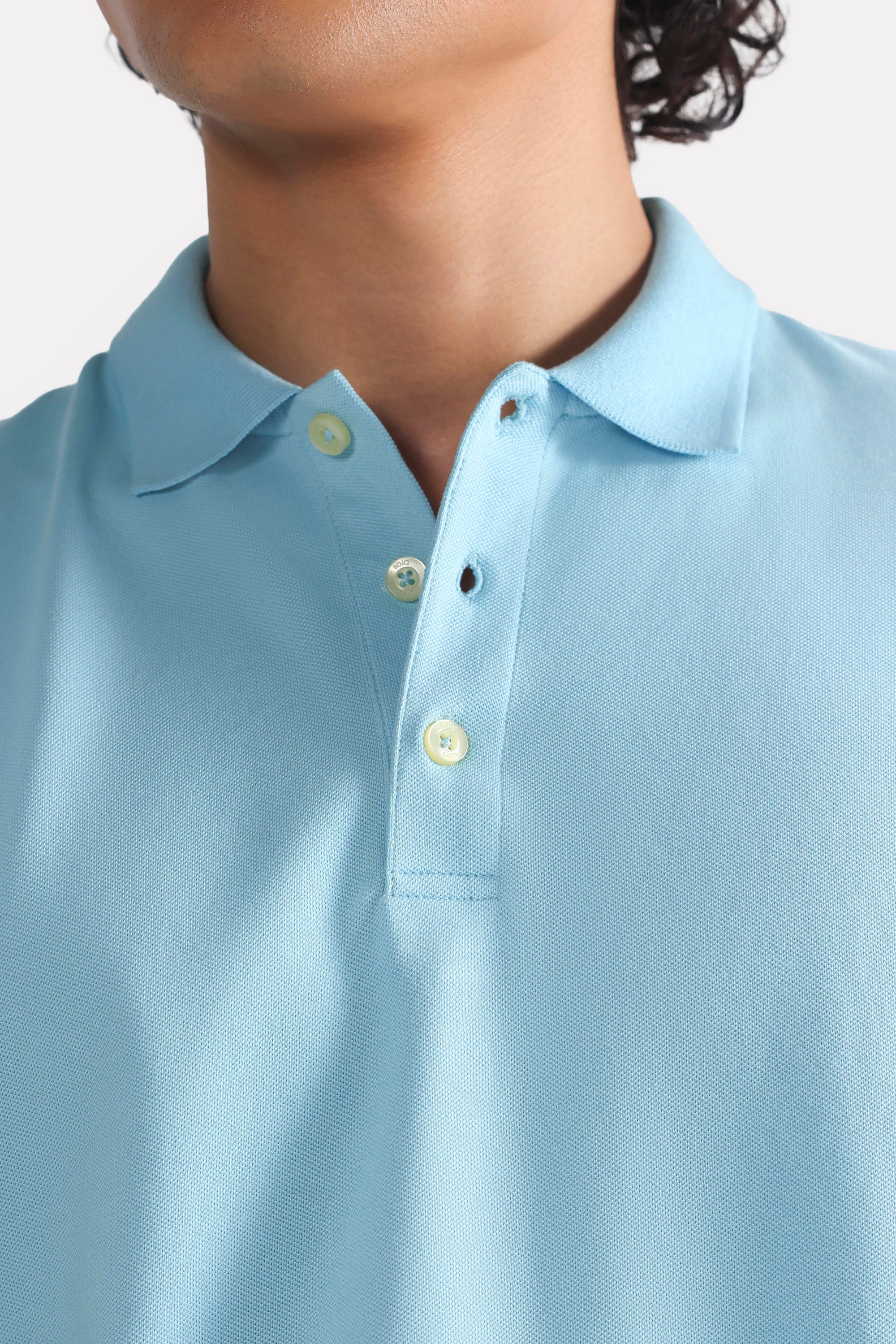 Close-up detail on the light blue micro-textured cotton pique polo, by SOLA Pakistan.