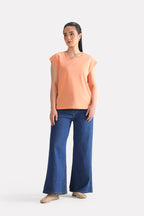 Close-up detail on the peach (apricot) relaxed shoulder-tab t-shirt, by SOLA Pakistan.